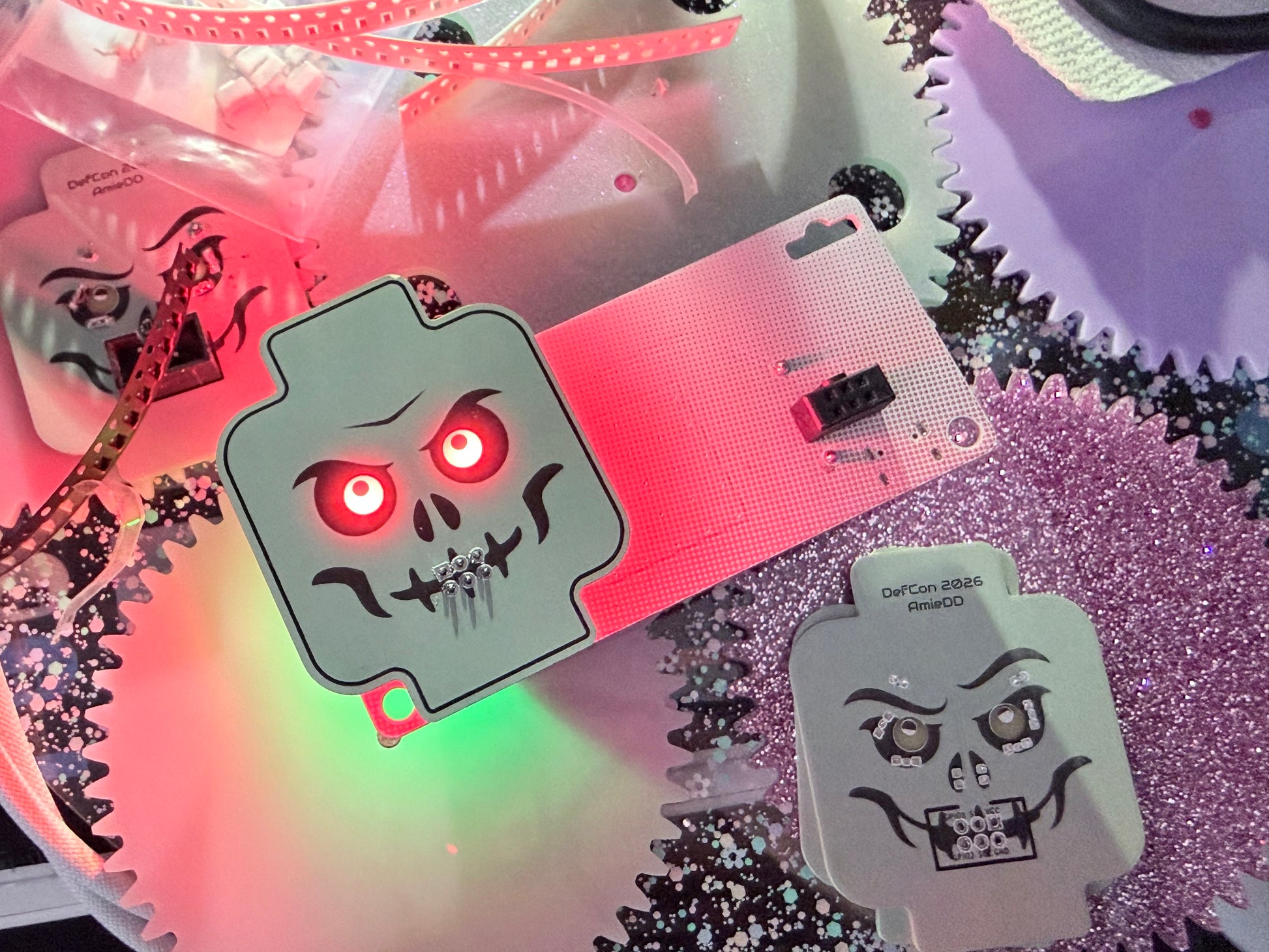 Assembled skeleton minifig-inspired DefCon SAO PCB with glowing red LED eyes next to an unassembled bare PCB showing the reverse side and 6-pin SAO connector footprint.